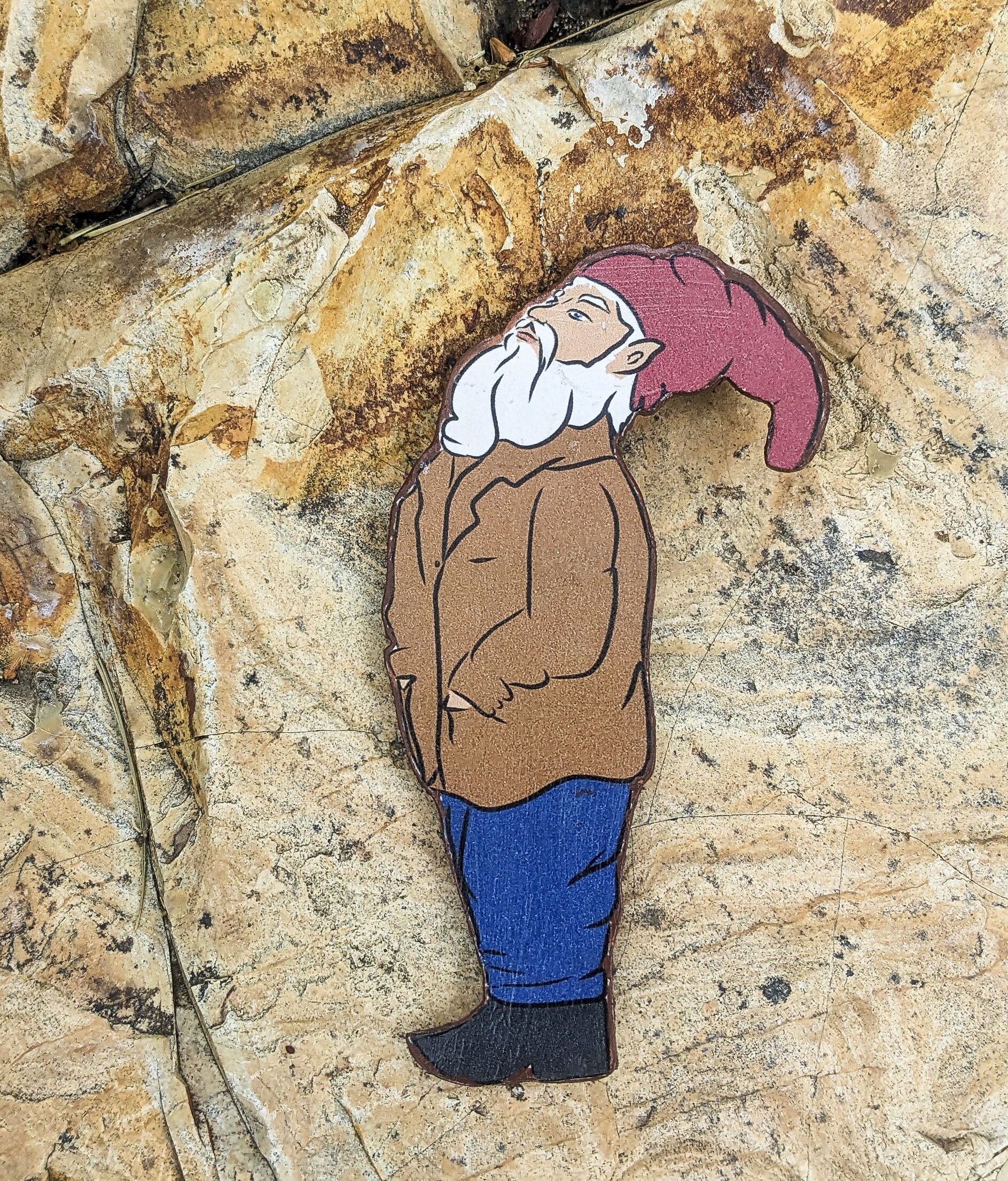Flat lay of wooden gnome magnet on natural surface — handmade wood cutout gift.