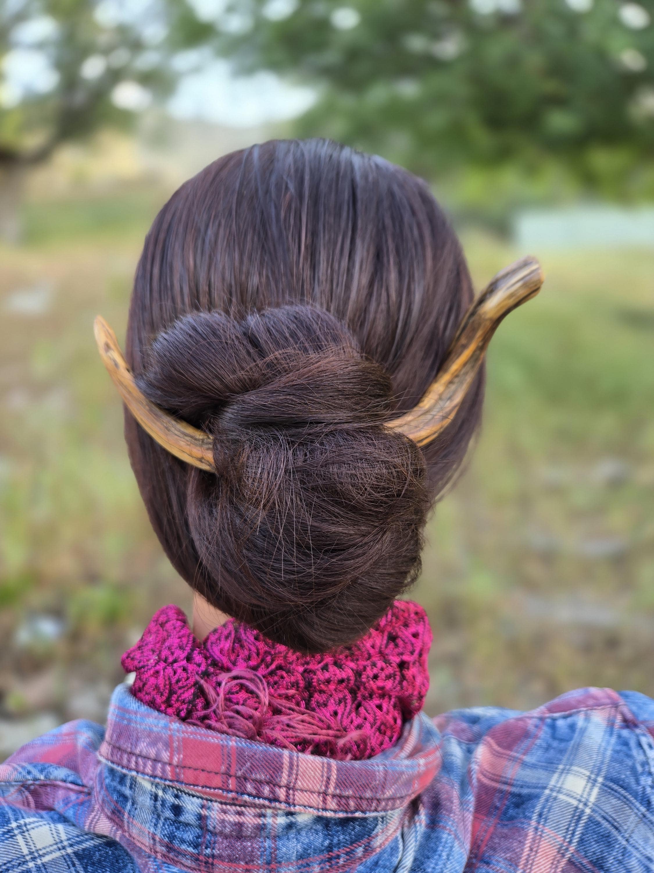 Hand-carved twisted wood hair fork securing a bun in long hair outdoors — plastic-free natural hairpin from Sprouted Dreams.
